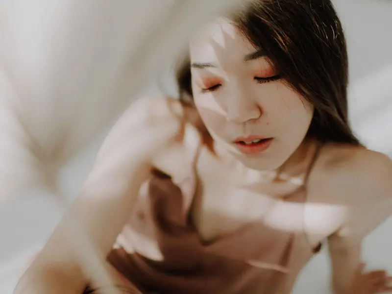 Mulher de olhos fechados em luz suave, com sombras delicadas sobre o rosto