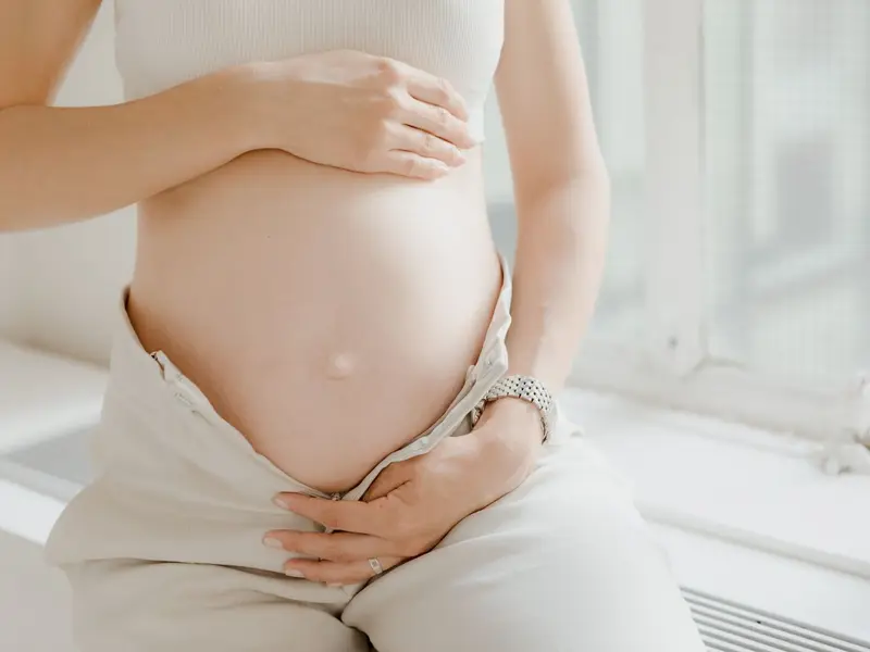 Gestante de roupas claras com as mãos sobre a barriga, em luz natural