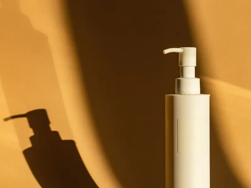 Frasco de loção com válvula pump projetando sombra em parede cor de mostarda