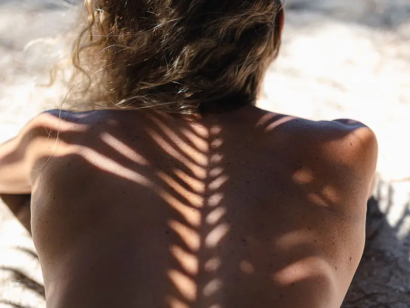 Costas de uma pessoa com sombra de folhas de palmeira sob o sol de verão